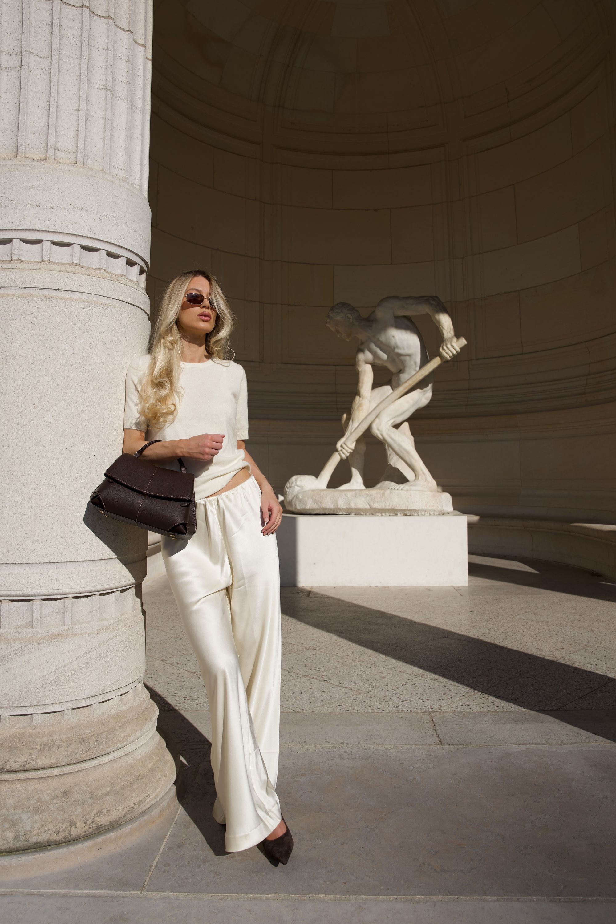 Fashion editorial portrait with a dark leather handbag beside a stone column